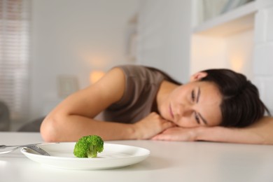 Photo of Eating disorder. Sad woman at white table, focus on broccoli and cutlery