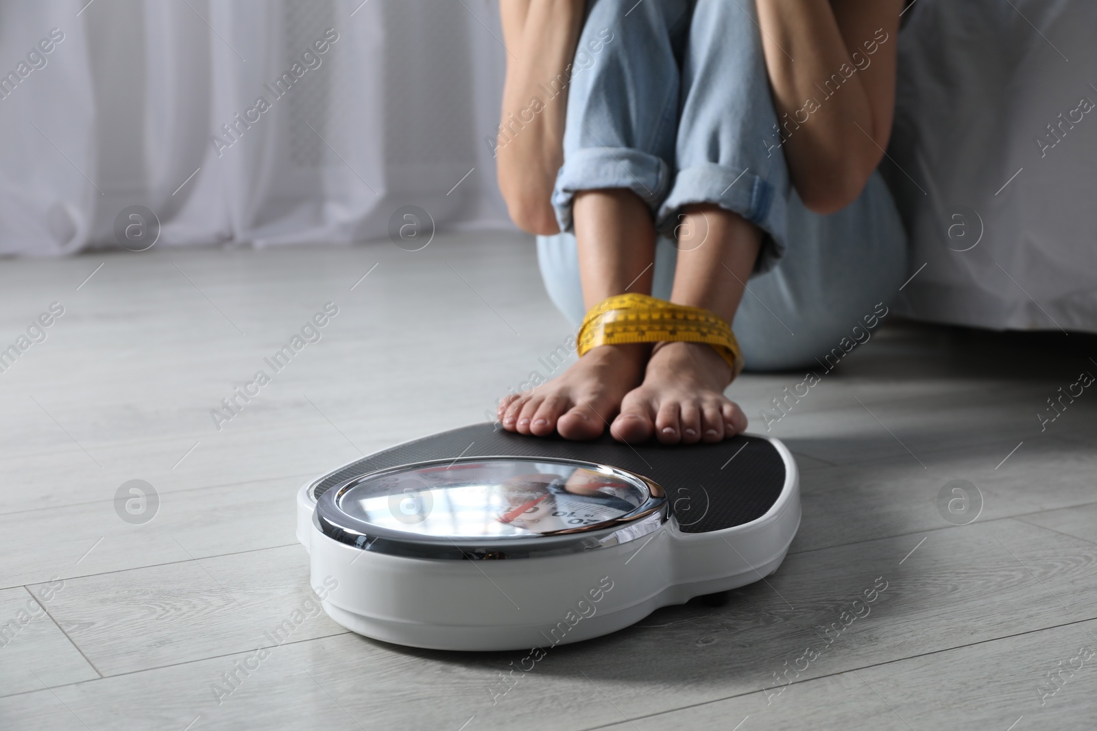 Photo of Eating disorder. Woman sitting near scale on floor indoors, closeup