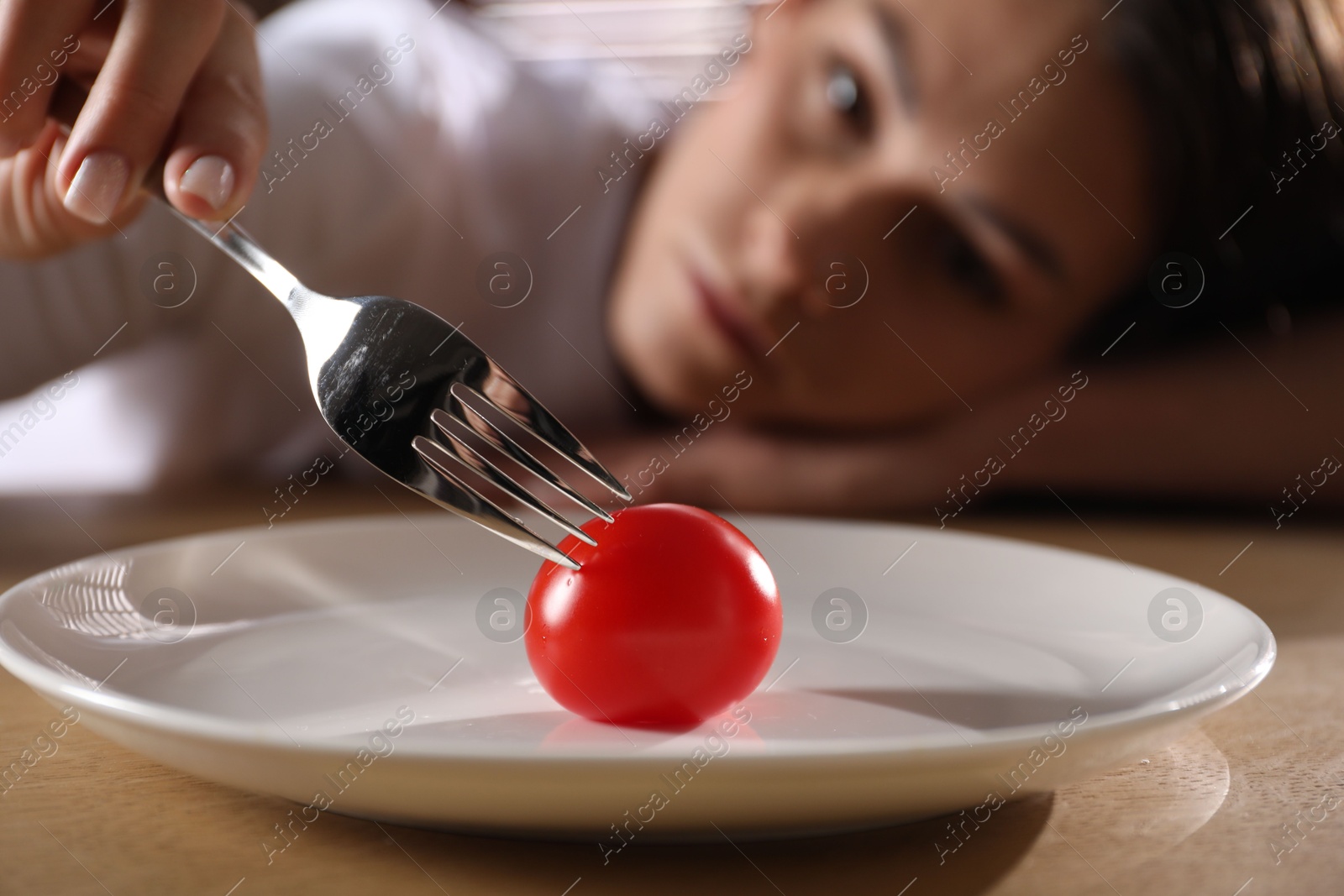 Photo of Eating disorder. Sad woman holding fork with tomato at wooden table indoors, selective focus