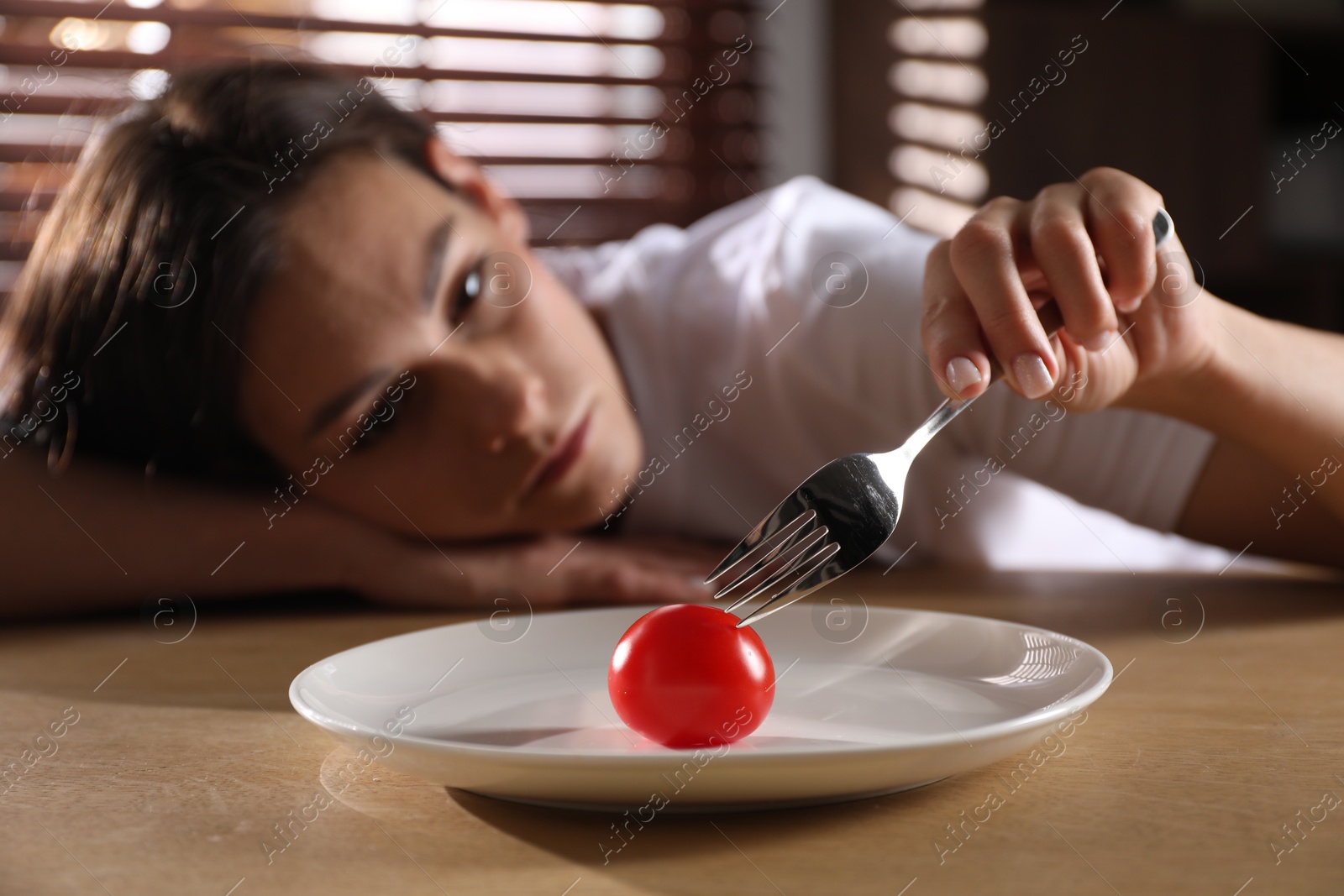 Photo of Eating disorder. Sad woman holding fork with tomato at wooden table indoors, selective focus