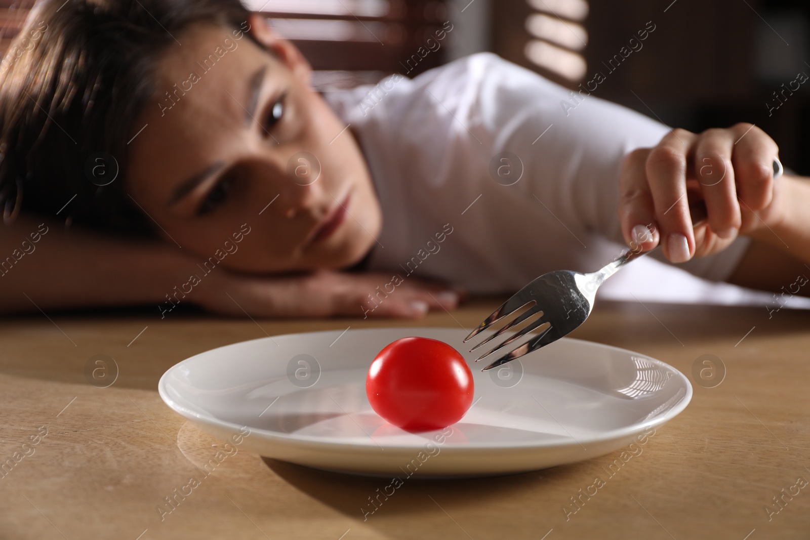 Photo of Eating disorder. Sad woman holding fork with tomato at wooden table indoors, selective focus