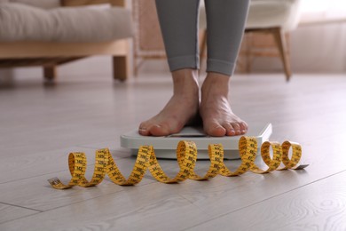 Eating disorder. Woman standing on floor scale and measuring tape indoors, closeup