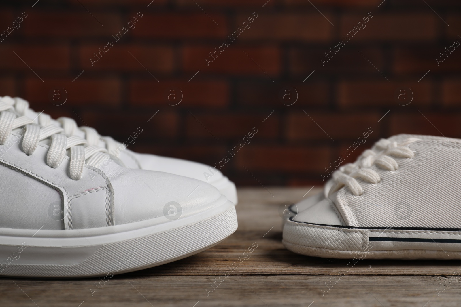 Photo of Big and small sneakers on wooden surface, closeup