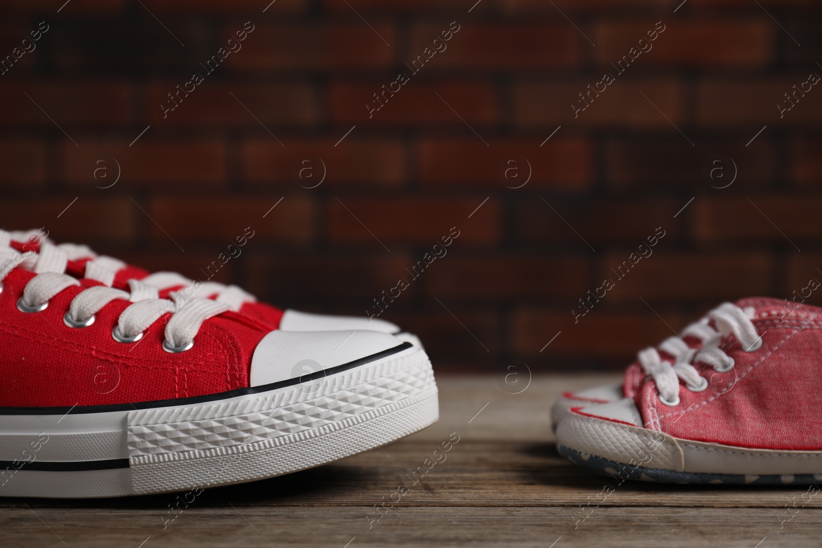 Photo of Big and small sneakers on wooden surface, closeup