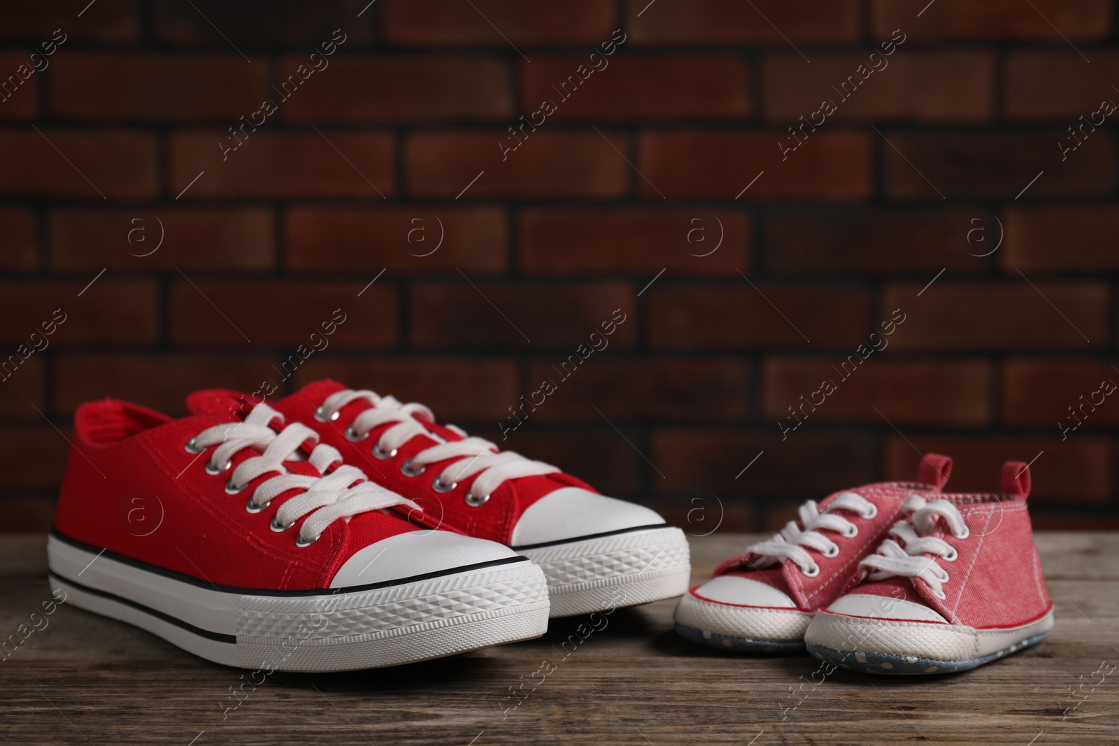 Photo of Big and small sneakers on wooden surface