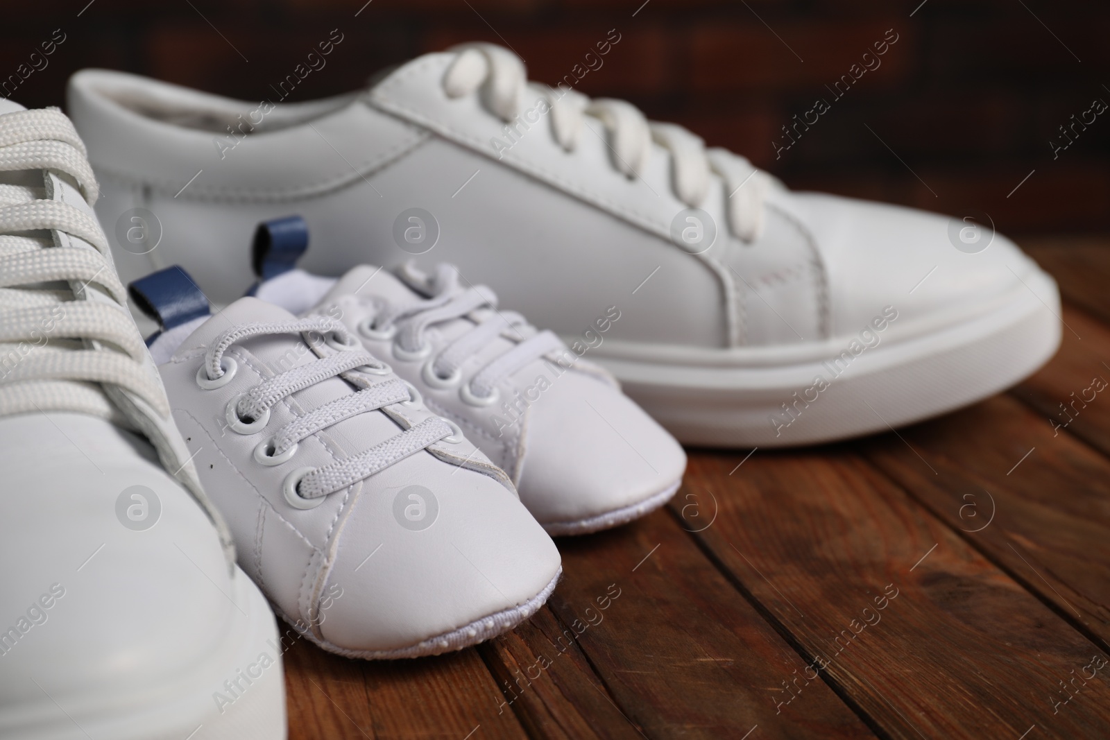 Photo of Big and small sneakers on wooden surface, closeup