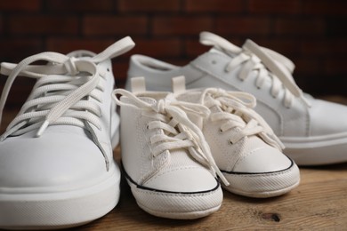 Photo of Big and small sneakers on wooden surface, closeup