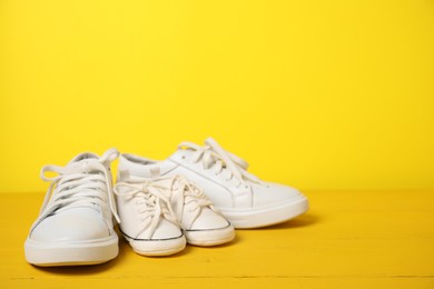 Photo of Big and small sneakers on yellow background. Space for text