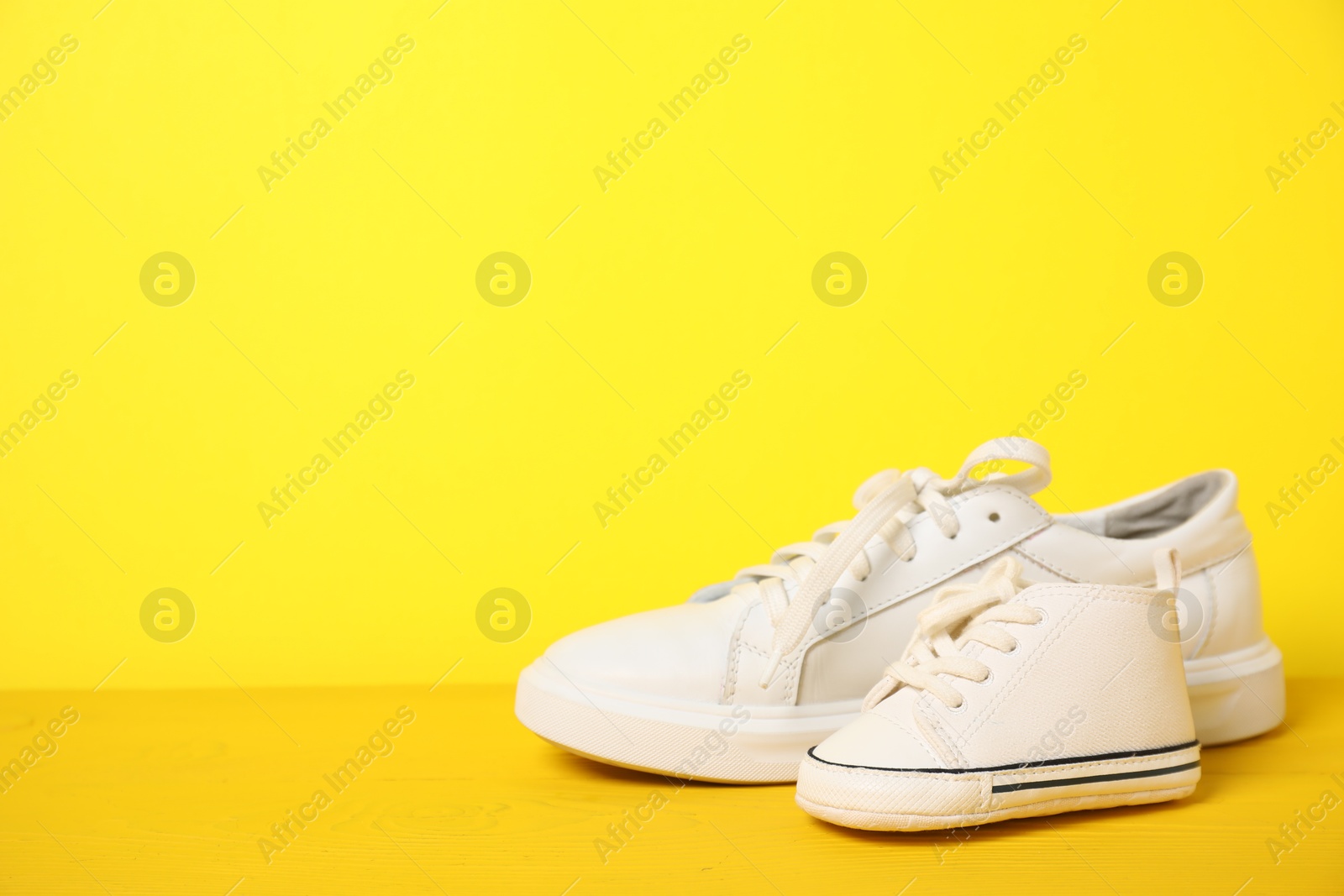 Photo of Big and small sneakers on yellow background. Space for text