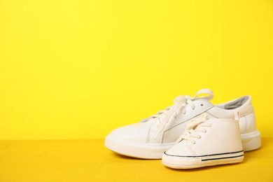 Big and small sneakers on yellow background. Space for text