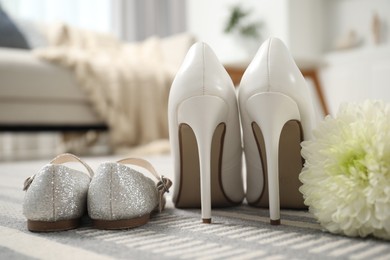 Photo of Big and small shoes with chrysanthemum flower on carpet