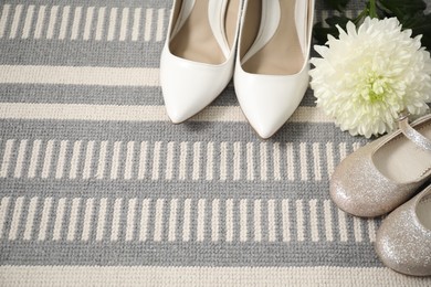 Photo of Big and small shoes with chrysanthemum flower on carpet, space for text