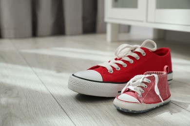 Photo of Big and small sneakers on floor indoors. Space for text