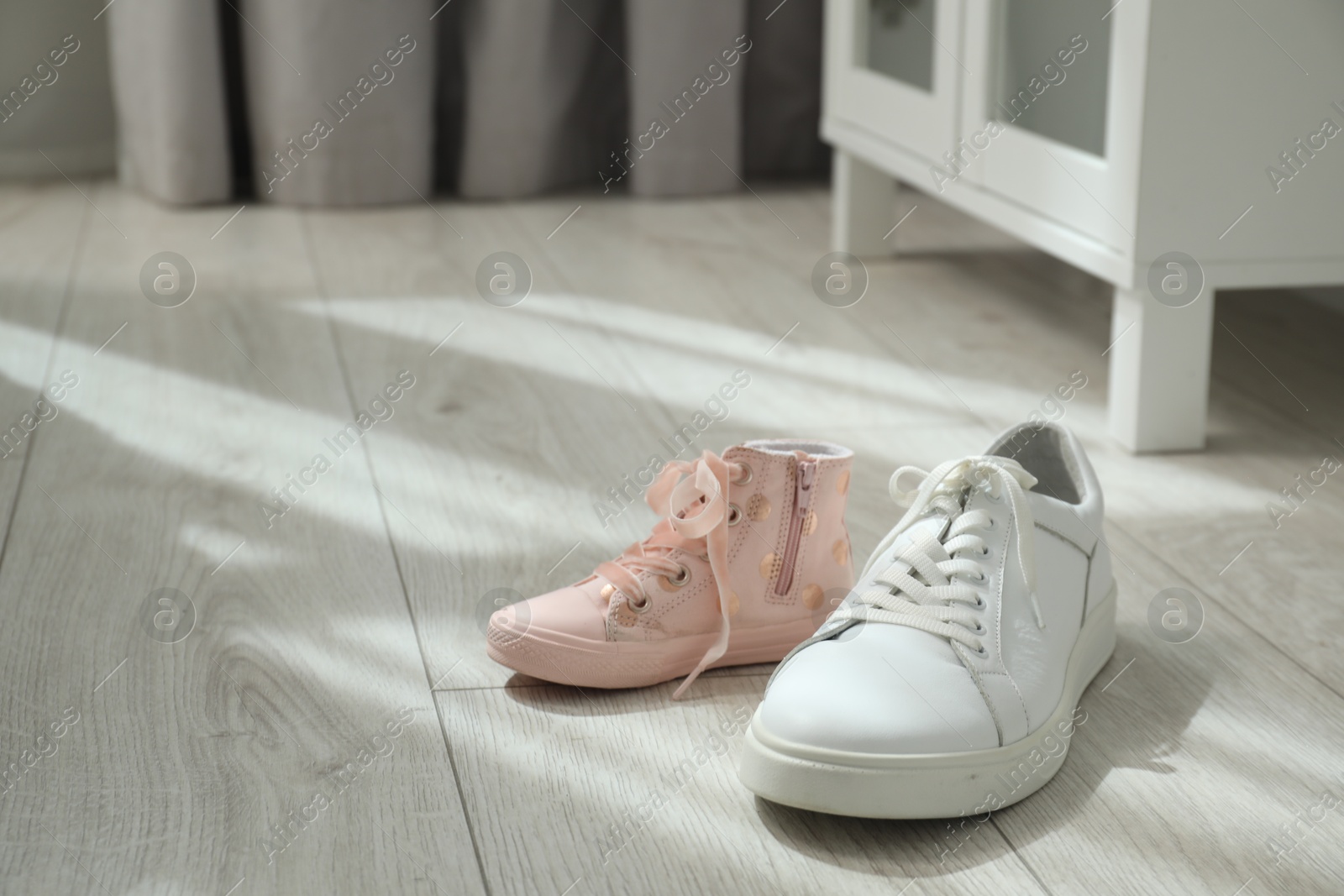 Photo of Big and small sneakers on floor indoors. Space for text