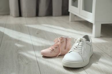 Photo of Big and small sneakers on floor indoors. Space for text