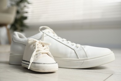 Photo of Big and small sneakers on floor indoors, closeup