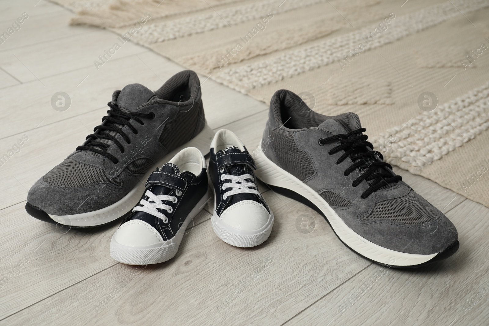 Photo of Big and small sneakers on wooden floor