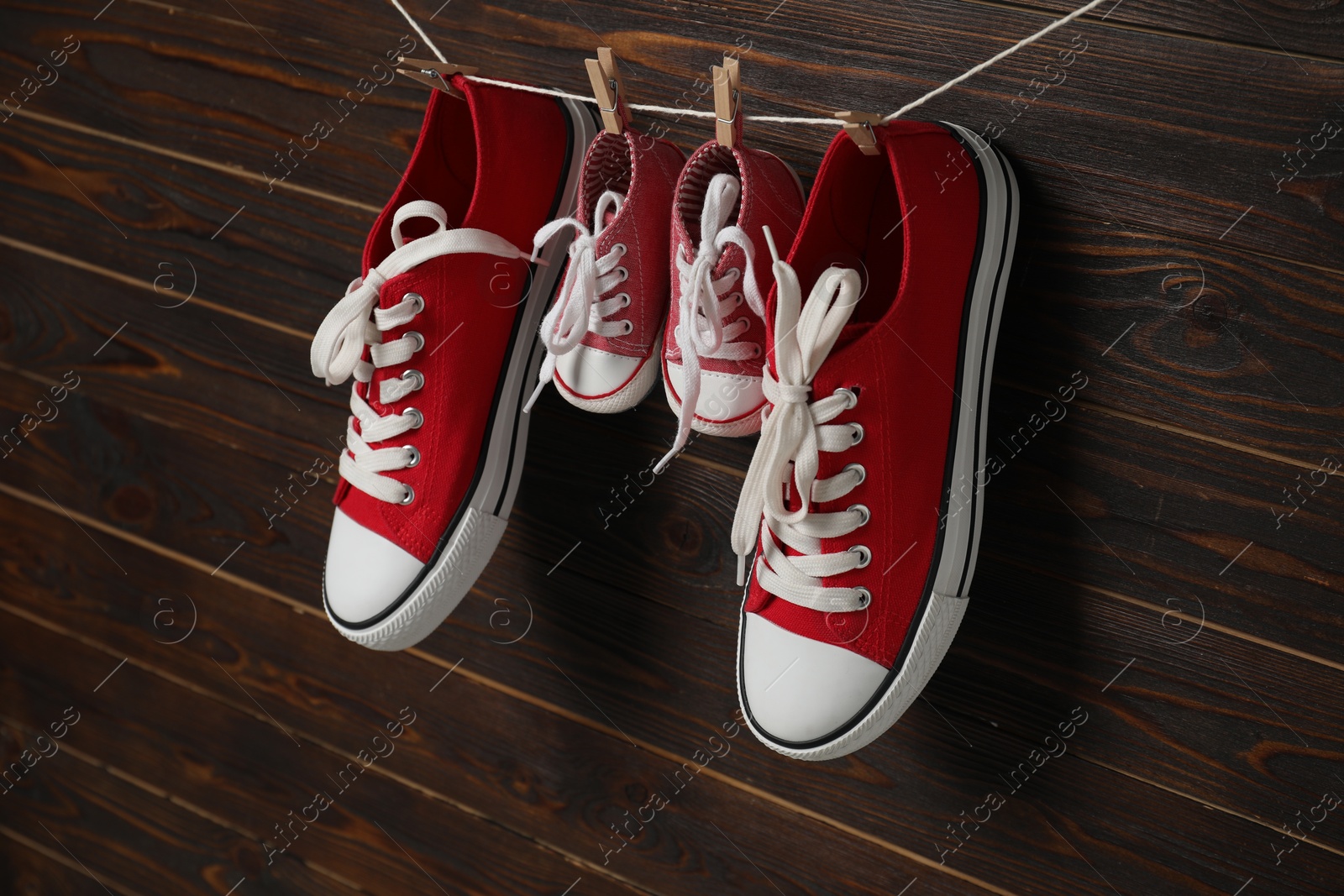 Photo of Big and small sneakers hanging on wooden background