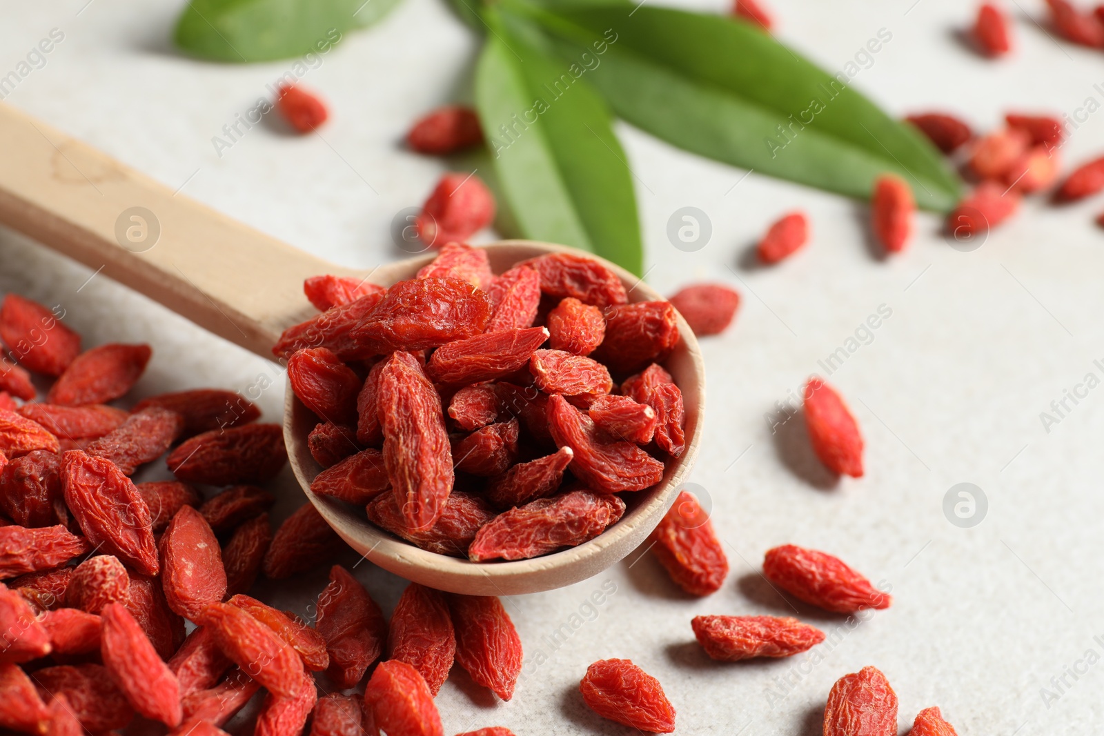 Photo of Dried goji berries and spoon on light table, closeup