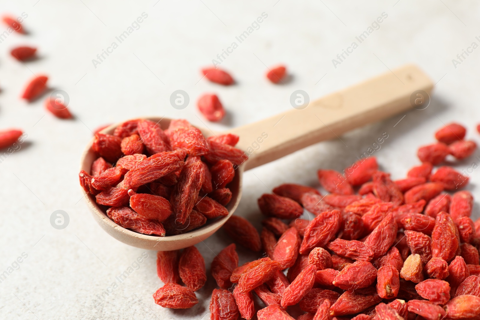 Photo of Dried goji berries and spoon on light table, closeup