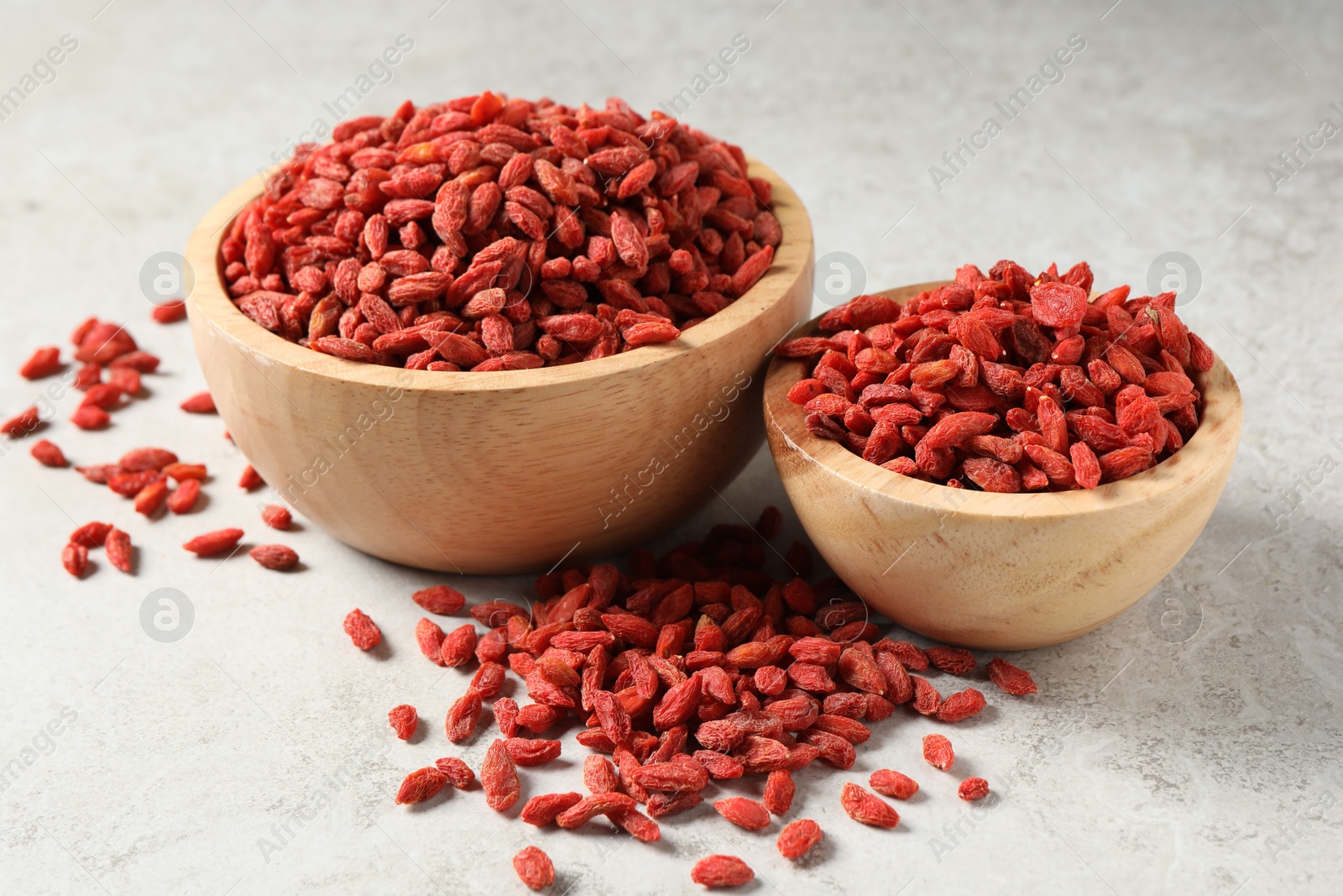 Photo of Dried goji berries in bowls on light textured table, closeup