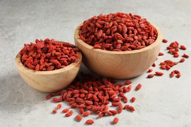 Photo of Dried goji berries in bowls on light textured table, closeup