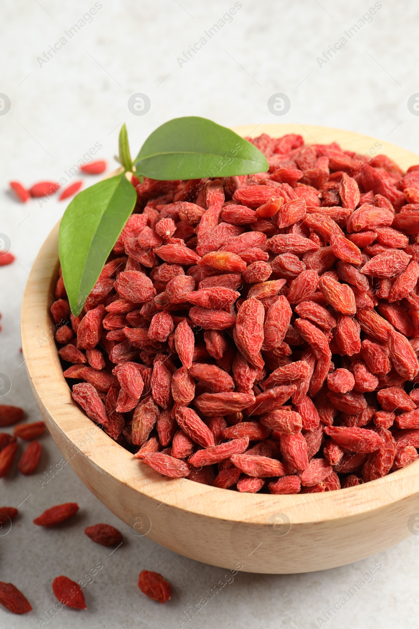 Photo of Dried goji berries and leaves in bowl on light textured table, closeup