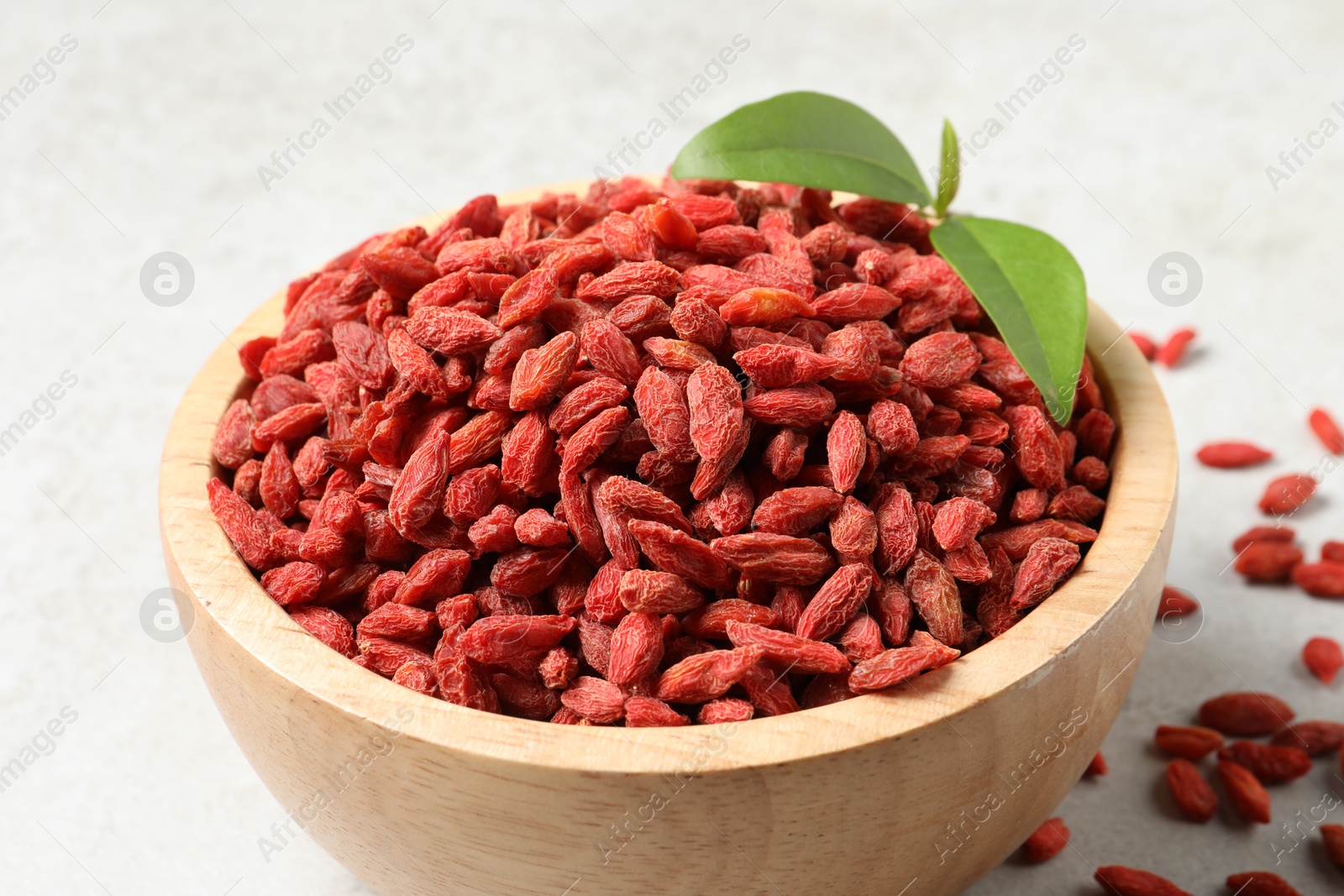 Photo of Dried goji berries and leaves in bowl on light textured table, closeup