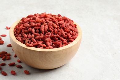 Dried goji berries in bowl on light textured table, closeup. Space for text