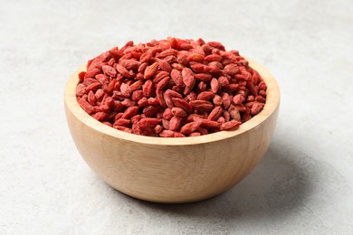 Dried goji berries in bowl on light textured table, closeup