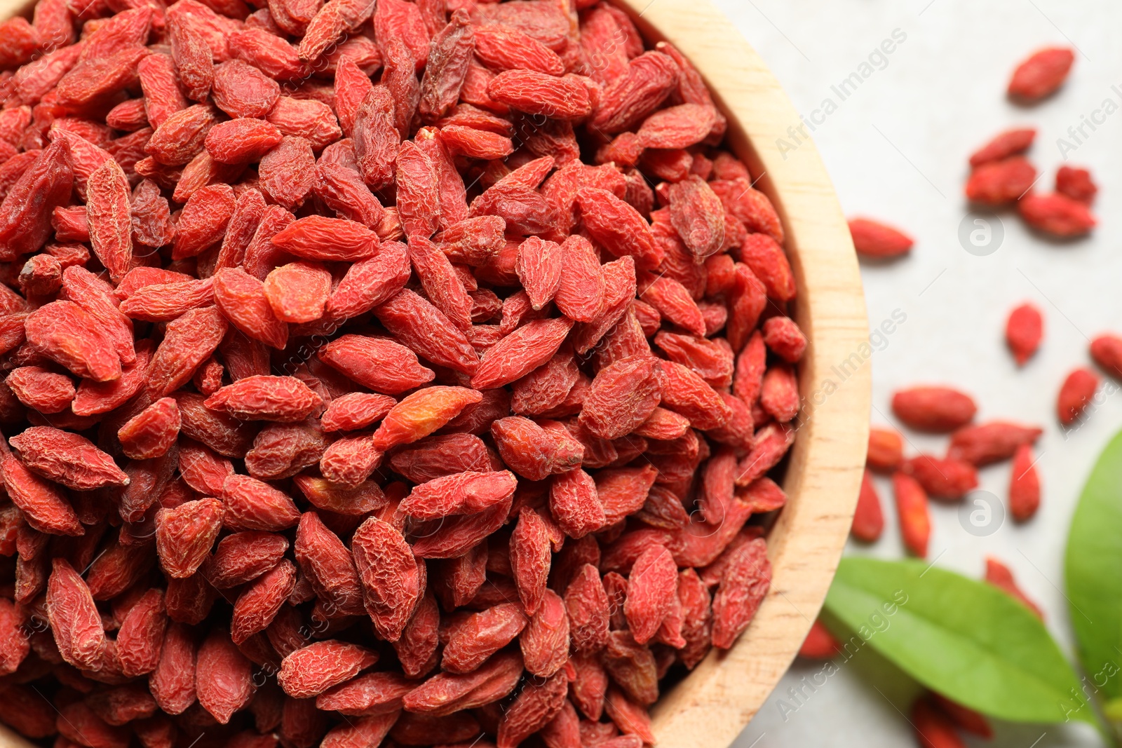 Photo of Dried goji berries in bowl on light table, flat lay