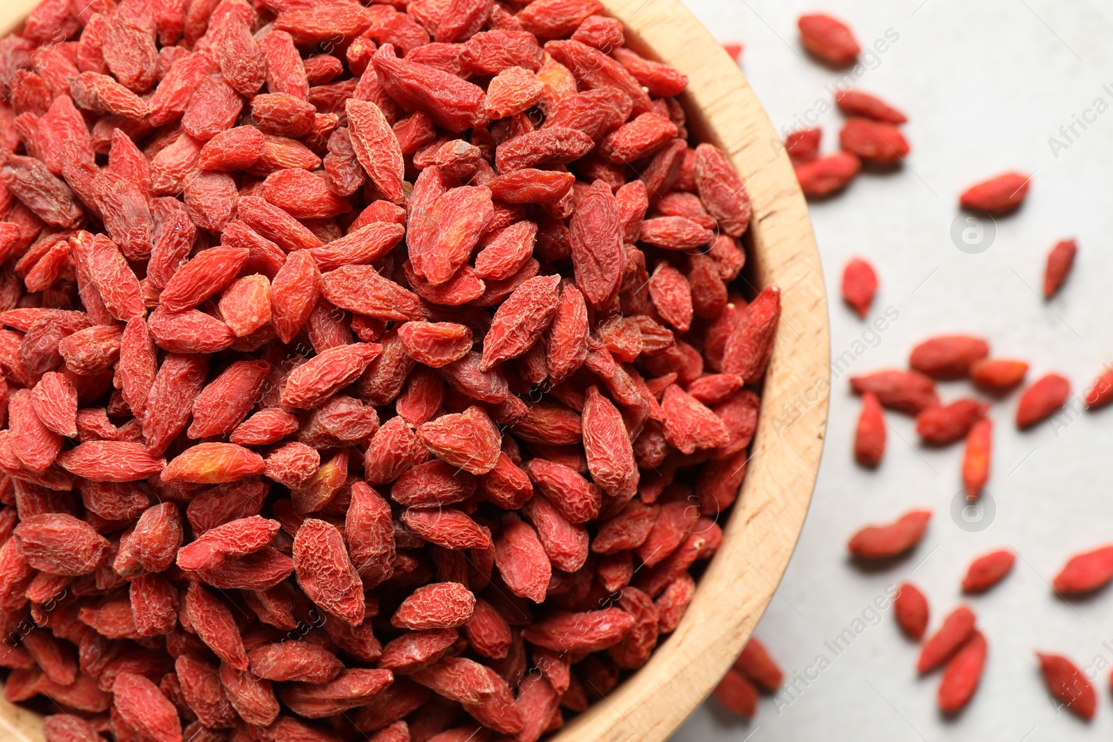 Photo of Dried goji berries in bowl on light table, flat lay