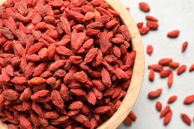 Dried goji berries in bowl on light table, flat lay