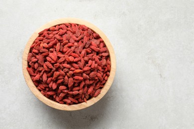 Photo of Dried goji berries in bowl on light textured table, top view. Space for text