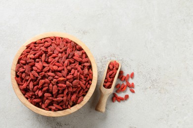 Photo of Dried goji berries in bowl and scoop on light textured table, flat lay. Space for text