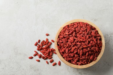 Dried goji berries in bowl on light textured table, top view. Space for text