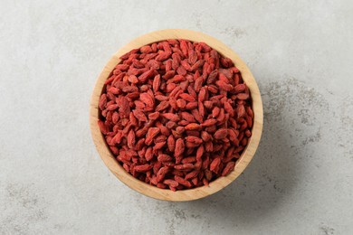 Dried goji berries in bowl on light textured table, top view