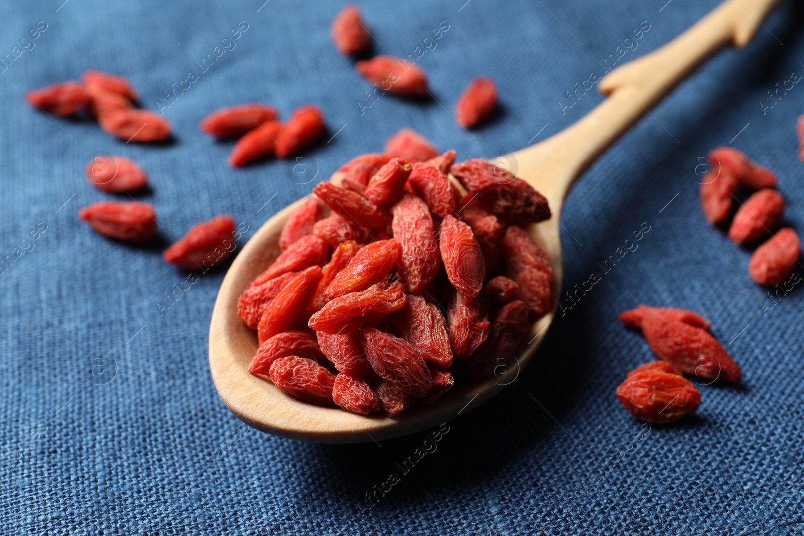 Photo of Spoon with dried goji berries on blue cloth, closeup