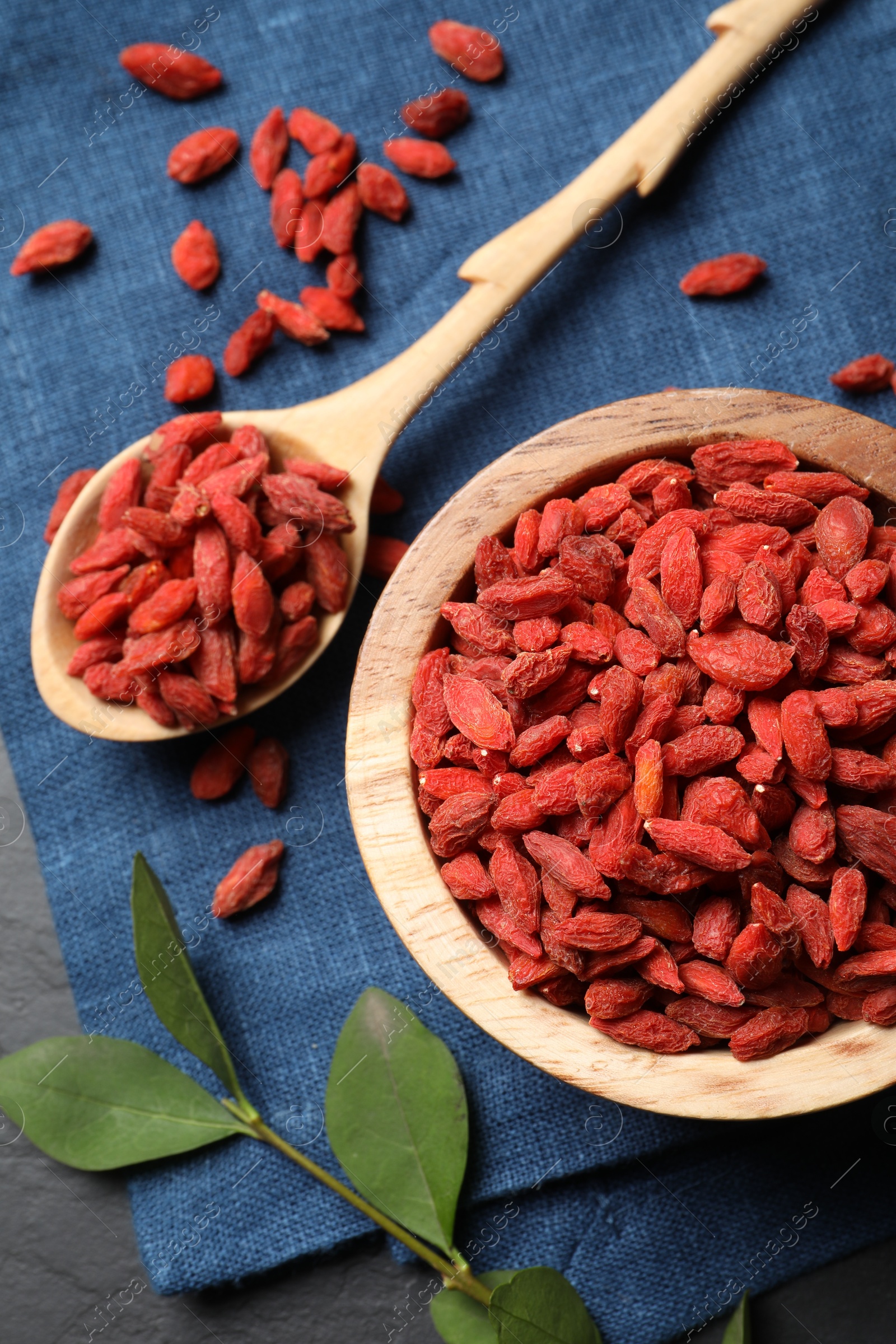 Photo of Dried goji berries and leaves on dark textured table, top view