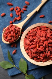 Dried goji berries and leaves on dark textured table, top view