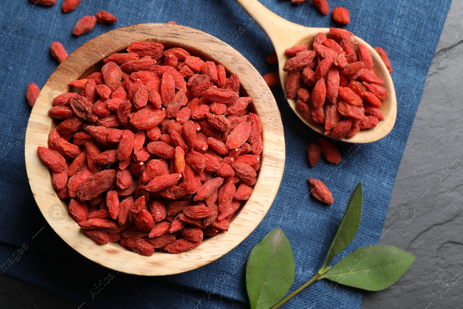 Photo of Dried goji berries and leaves on dark textured table, top view