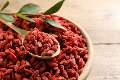 Dried goji berries in bowl and spoon on wooden table, closeup. Space for text
