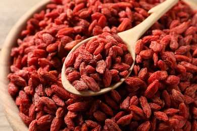 Photo of Dried goji berries in bowl and spoon on table, closeup