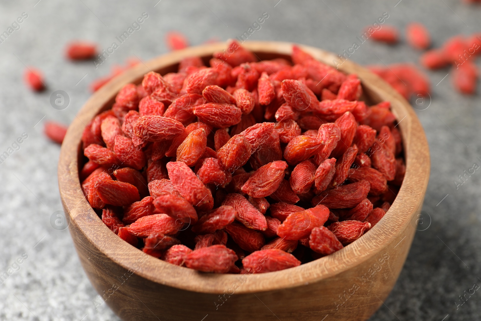 Photo of Dried goji berries in bowl on grey textured table, closeup