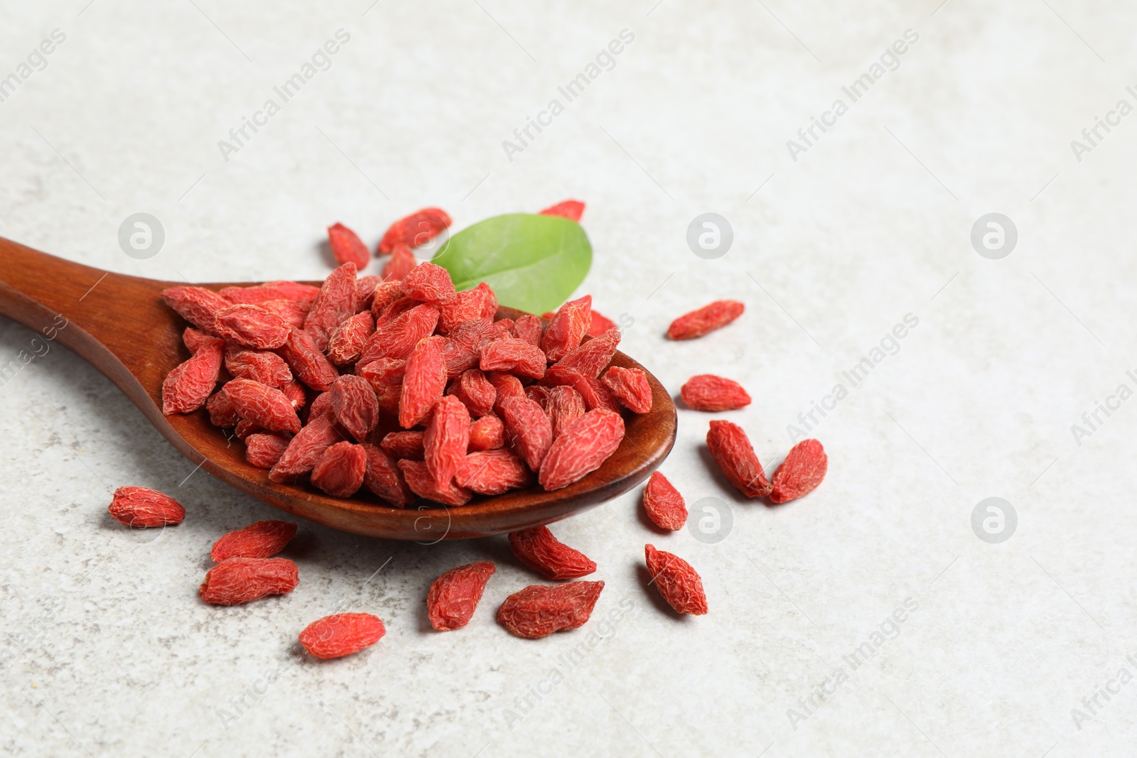 Photo of Dried goji berries and spoon on light textured table, closeup