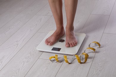 Photo of Eating disorder. Woman standing on floor scale and measuring tape indoors, closeup. Space for text