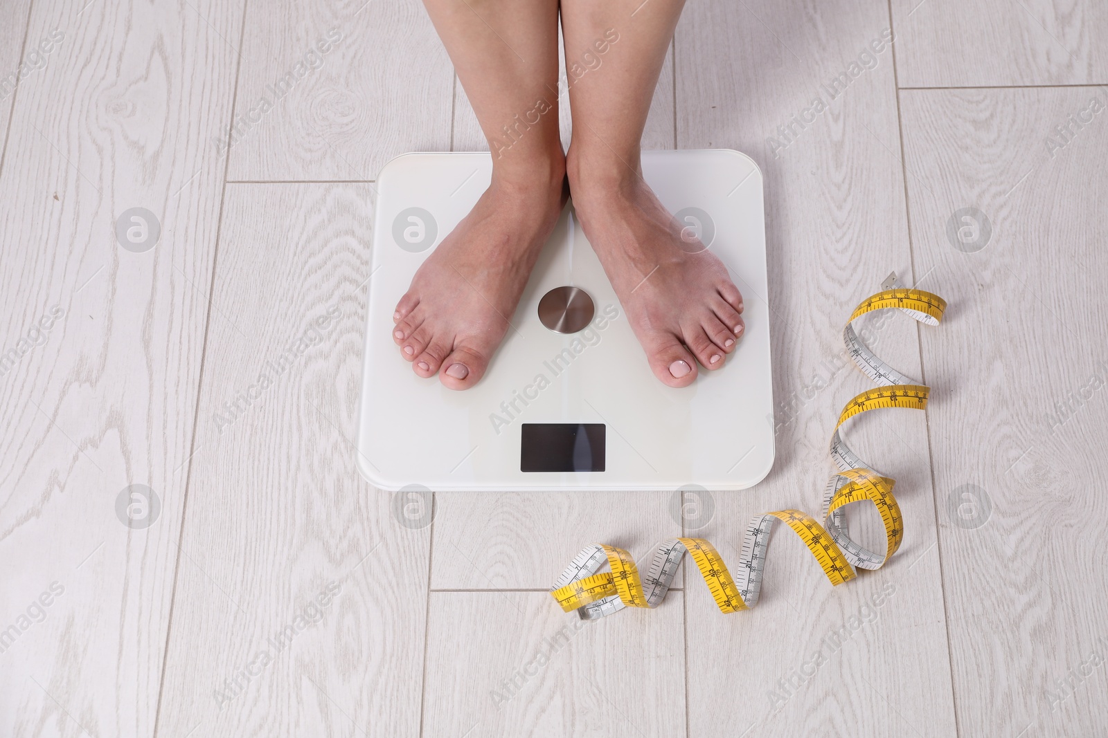 Photo of Eating disorder. Woman standing on floor scale and measuring tape indoors, above view