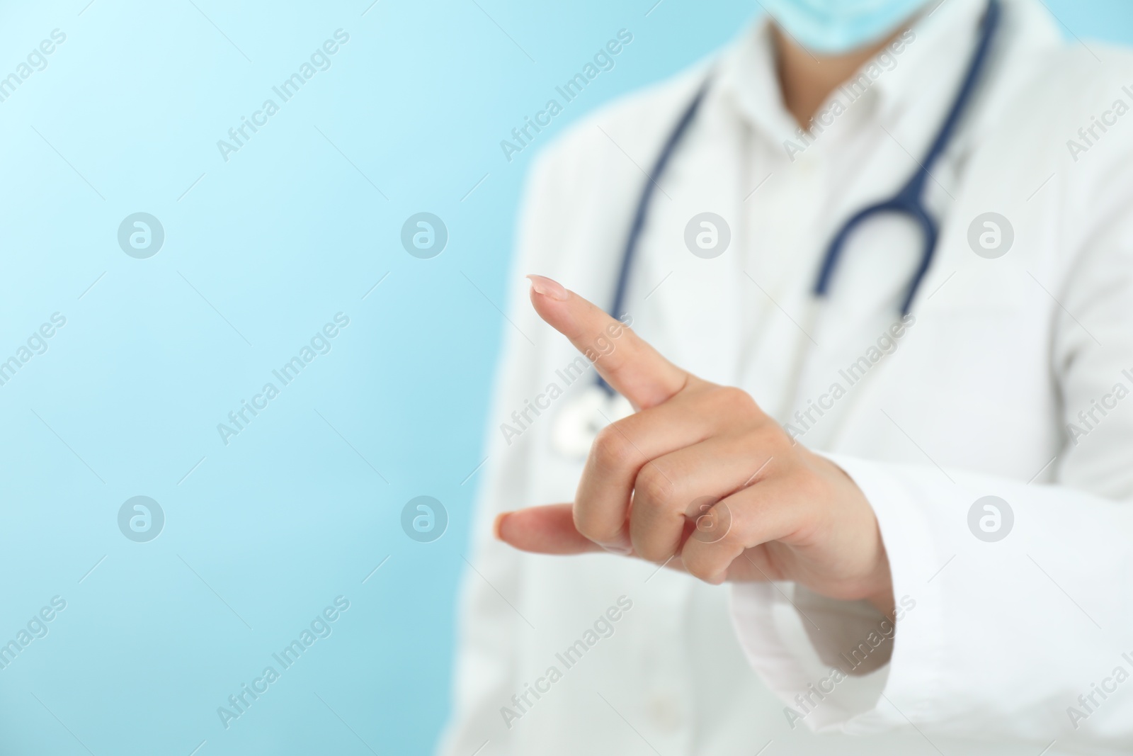 Photo of Doctor pointing at something on light blue background, closeup. Space for text