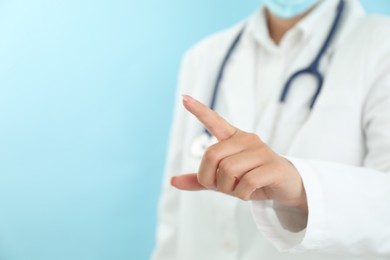 Photo of Doctor pointing at something on light blue background, closeup. Space for text