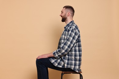 Man with good posture sitting on chair against pale orange background